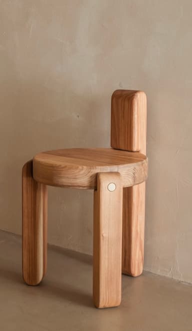 A minimalist, light-toned wood chair featuring a circular seat and a short, rectangular backrest. The design is characterized by thick, rounded elements for the legs and back, giving it a sculptural and contemporary appearance with visible wood grain. — 3D model