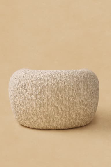 An eccentric upholstered armchair featuring a rounded, organic form and four dark wooden legs sculpted to resemble high-heeled boots. The chair is covered in a textured, light beige boucle fabric, providing a soft and inviting appearance. The design is whimsical and sculptural, making it a distinctive statement piece. — 3D model