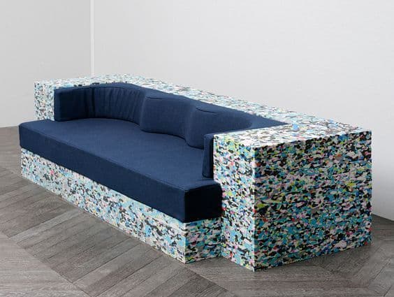 A modular sofa with a distinct construction. The base and armrests are composed of compressed, multi-colored foam or recycled materials, creating a textured, pixelated appearance. The seating and back cushions are upholstered in a dark blue fabric. — 3D model
