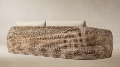 A contemporary sofa featuring a curved, open-weave rattan frame and soft, light-colored upholstered cushions on the seat and back. — 3D model