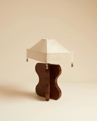 A table lamp featuring a distinctive sculpted wooden base in a dark finish and a rectangular, tapered fabric shade with pleated details and decorative tassels at the corners. The base exhibits an organic, hourglass-like form. — 3D model