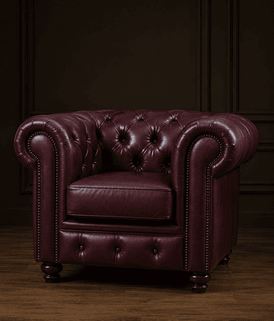 A classic Chesterfield-style armchair upholstered in deep red or burgundy leather, featuring characteristic deep button tufting on the backrest and rolled arms. The front facade of the arms and the lower front panel of the chair are adorned with decorative brass nailhead trim. It sits on four turned, dark wood feet. — 3D model