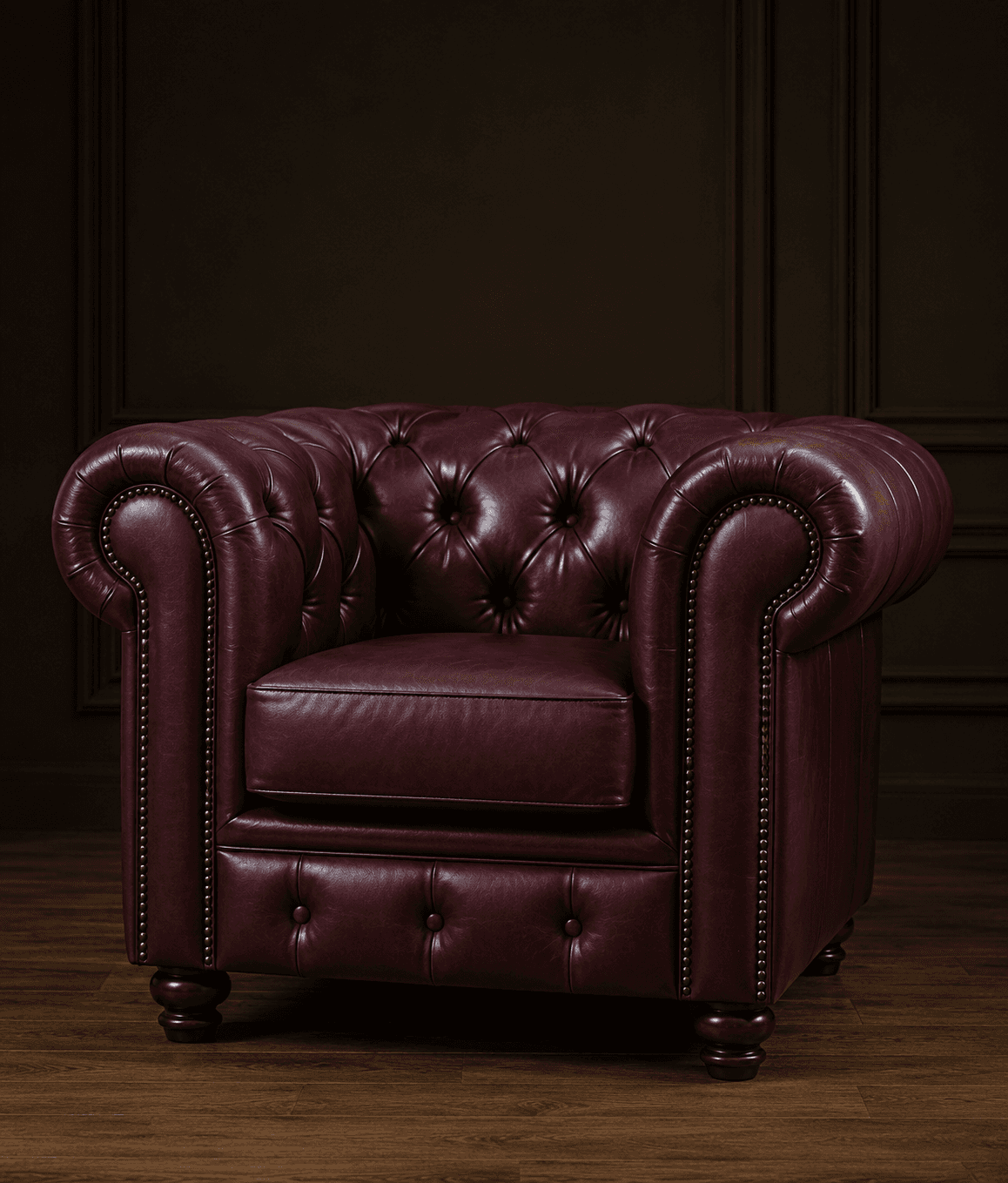 A classic Chesterfield-style armchair upholstered in deep red or burgundy leather, featuring characteristic deep button tufting on the backrest and rolled arms. The front facade of the arms and the lower front panel of the chair are adorned with decorative brass nailhead trim. It sits on four turned, dark wood feet. — 3D model
