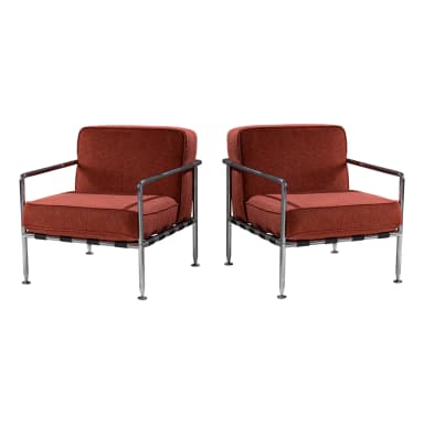 An armchair with a chrome-plated tubular steel frame and upholstered cushions. The seat and back cushions are covered in a textured, rust-colored fabric. The frame consists of slender legs, armrests, and a horizontal back support. Black woven straps are visible underneath the seat, connecting the frame elements. — 3D model