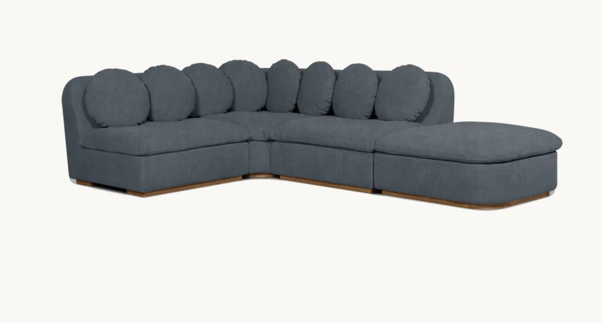 A contemporary sectional sofa with a chaise lounge extension. The sofa features a modular design with individual seating units. It is upholstered in a textured dark gray fabric and has multiple round, bolster-style back cushions. The base is elevated by a low-profile wooden plinth. — 3D model