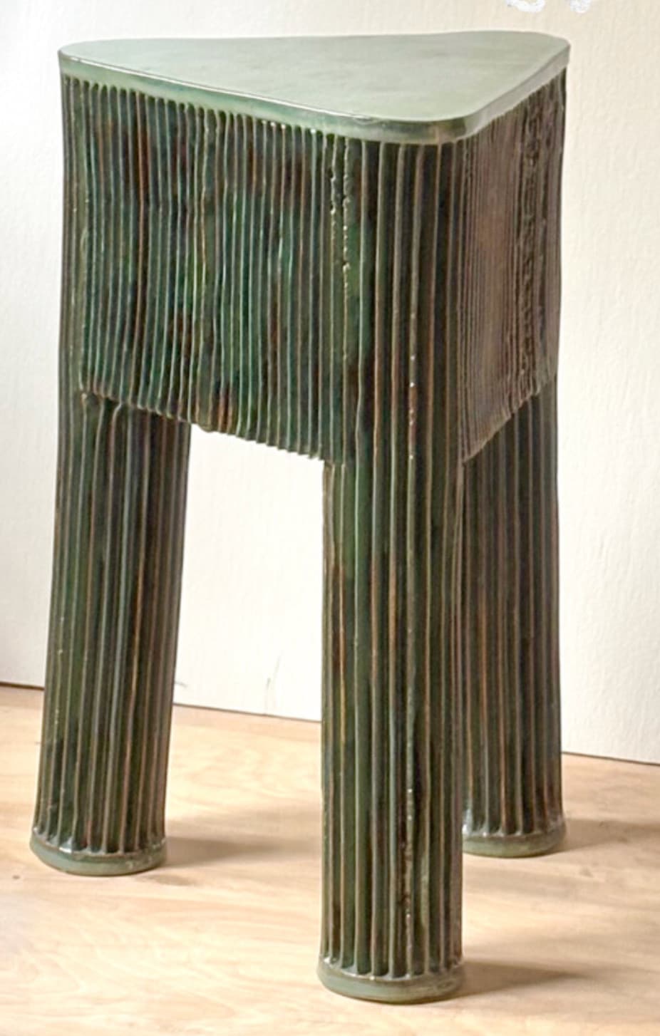 A triangular side table with a textured, ribbed surface on its vertical sides and legs. It has three legs that are integral to the structure. The top surface appears smooth and flat. — 3D model