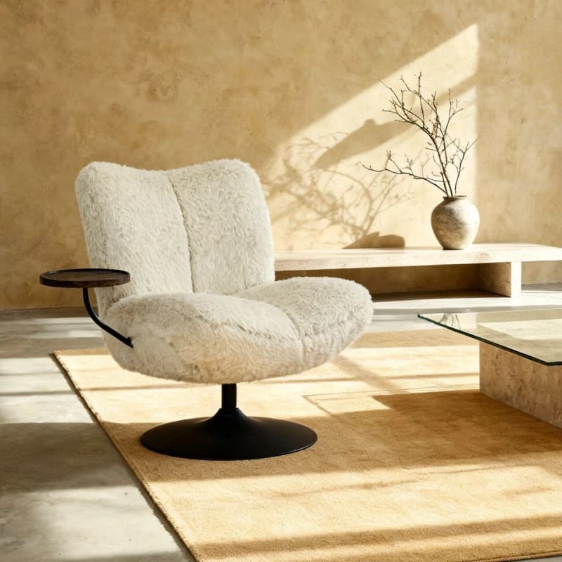 A plush, cream-colored armchair with a distinctive, textured upholstery that resembles sheepskin or faux fur. The chair features a low-profile, rounded silhouette with segmented cushions for the seat and back. It is mounted on a black, circular swivel base. A small, dark wooden circular side table is attached to the left side of the chair via a black metal arm. — 3D model