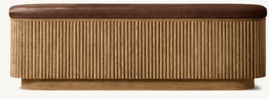 An elongated oval bench featuring a brown leather upholstered top and a base constructed from vertically reeded natural wood. The base maintains an oval form, slightly narrower than the top, and rests on a subtle plinth. — 3D model