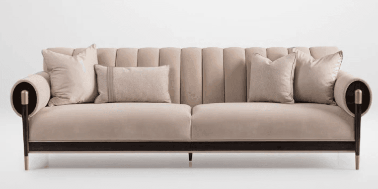 A sophisticated contemporary sofa featuring channel-tufted backrest cushions, plush seat cushions, and distinctive rolled cylindrical armrests. It is upholstered in a light beige or cream velvet fabric, complemented by a dark wood base and tapered legs with brass ferrule accents, giving it a luxurious and modern aesthetic. — 3D model