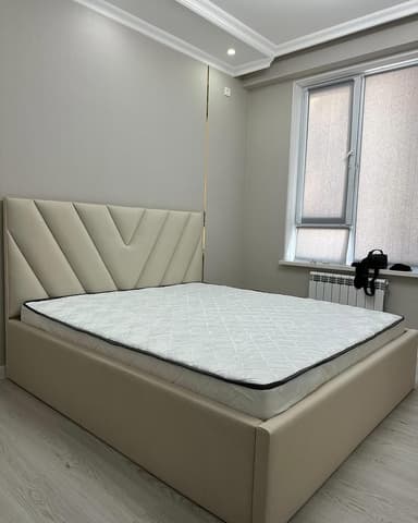A modern platform bed featuring a light beige upholstered frame and headboard. The headboard is adorned with a distinctive geometric tufting pattern, creating V-shaped or chevron lines. A white quilted mattress with a black trim is positioned on the integrated platform base. — 3D model