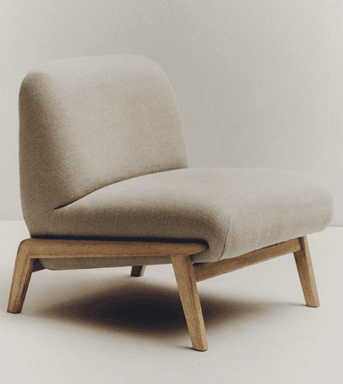 A low-profile armchair with a rounded, upholstered seat and backrest, supported by a minimalist wooden frame. The armchair features a fabric upholstery that appears to be a light beige or off-white color and a visible wooden base with four angled legs. — 3D model