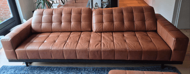 A modern three-seater sofa featuring brown leather upholstery with square tufting on the seat and back cushions. It is supported by a minimalist black metal frame with slender legs. — 3D model