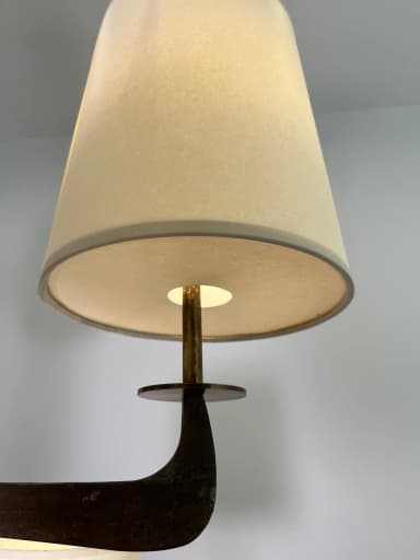 A modern multi-arm chandelier featuring a dark bronze-finished metal frame and eight tapered, drum-style fabric shades. The central column extends from a chain suspension, with eight arms branching out, each supporting an upward-facing light socket covered by a cream-colored textile shade. The metalwork exhibits a rustic or aged patina, suggesting a blend of modern design with traditional material treatment. — 3D model