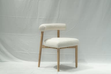 A contemporary side chair with a rounded backrest and seat upholstered in a textured, boucle fabric. The chair features a light-colored wooden frame with four tapered legs. The design is minimalist and modern. — 3D model