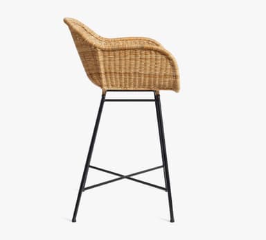 A bar stool featuring a natural woven rattan seat and backrest with integrated armrests, supported by a minimalist black metal frame with an X-shaped footrest. — 3D model