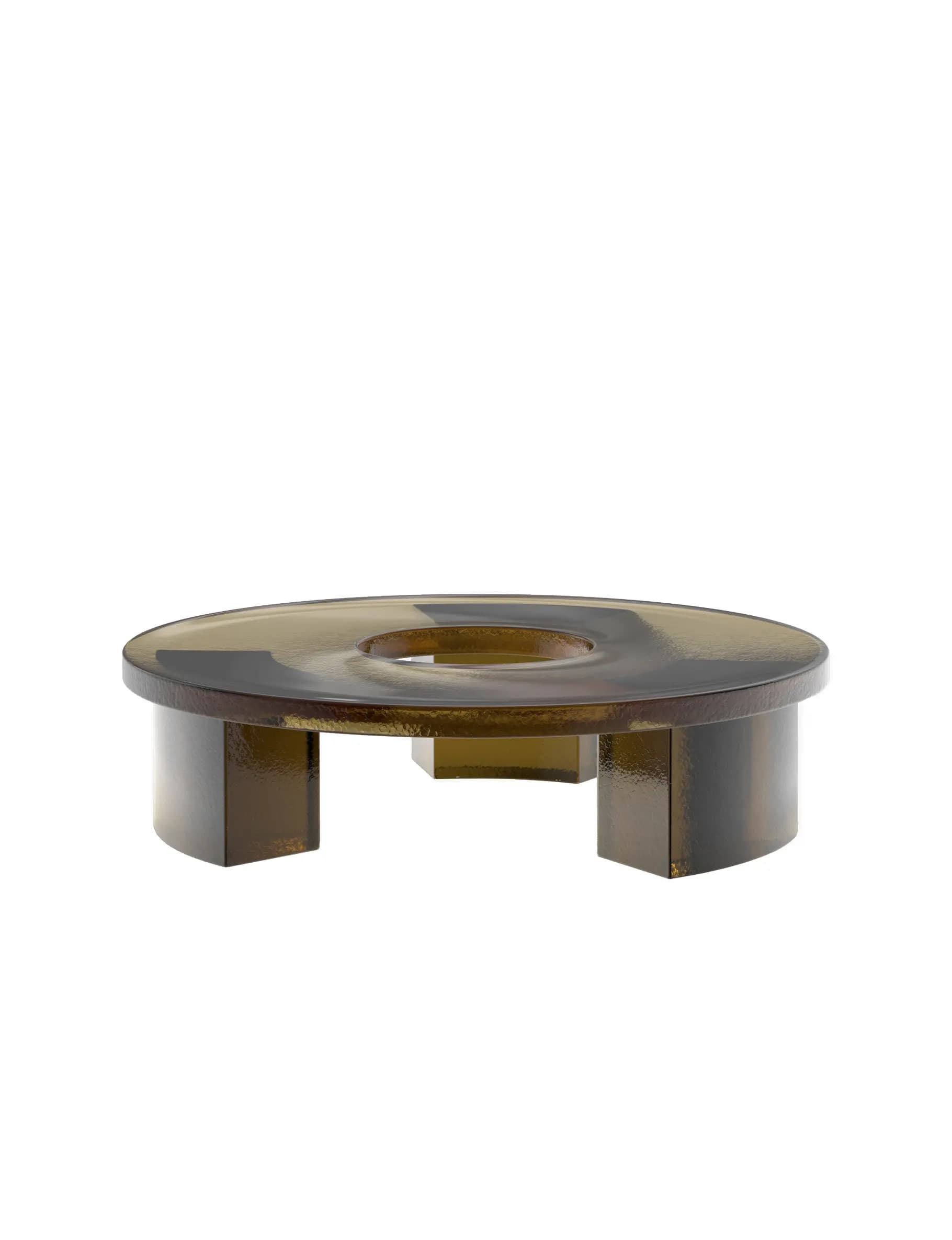 A low, circular table constructed from thick, translucent dark amber (smoked) glass. It features a flat, round top with a distinct central circular opening. The table is supported by several short, chunky, rectangular block legs integrated into the circular base. The entire surface has a textured or hammered finish, which refracts light and gives the material a unique, tactile quality. Its design is modern and sculptural. — 3D model
