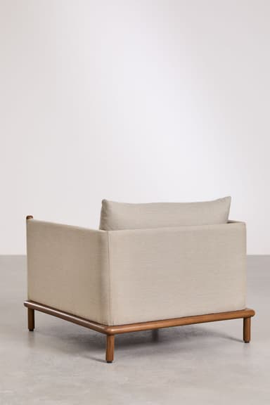 A modern lounge chair featuring a plush, upholstered body in a light beige/grey fabric set upon an exposed, warm-toned wooden base. The chair has a boxy, minimalist design with integrated, low armrests and a loose, rectangular back cushion. The slender, cylindrical wooden legs are slightly splayed, providing stability and contributing to the chair's contemporary aesthetic. — 3D model