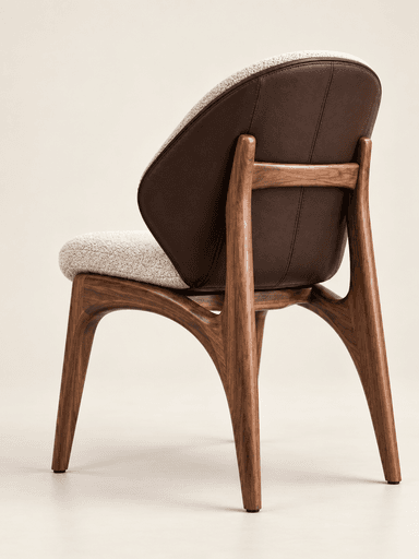 A modern, sculptural chair featuring a dark brown, organically curved walnut wood frame. The seat and inner backrest are upholstered in a light, textured bouclé fabric, while the outer backrest is covered in a smooth, contrasting dark brown material, possibly leather or faux leather. The chair has no visible armrests and stands on four tapered legs that flow seamlessly from the main frame. — 3D model