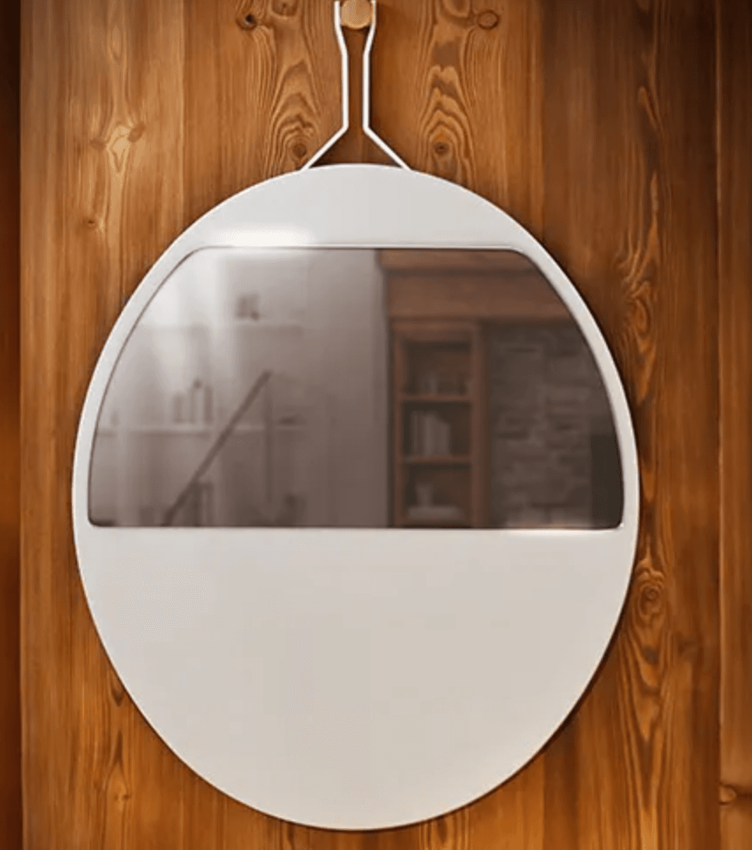 A wall-mounted mirror with a distinctive shape. The mirror has a large, predominantly white frame that is widest at the bottom and tapers towards the top. The reflective surface is positioned in the upper half of the object, appearing to be a convex or curved mirror. A thin, white strap with a small wooden peg attaches to the top center of the frame, suggesting a hanging mechanism. The mirror is mounted on a wooden paneled wall. — 3D model