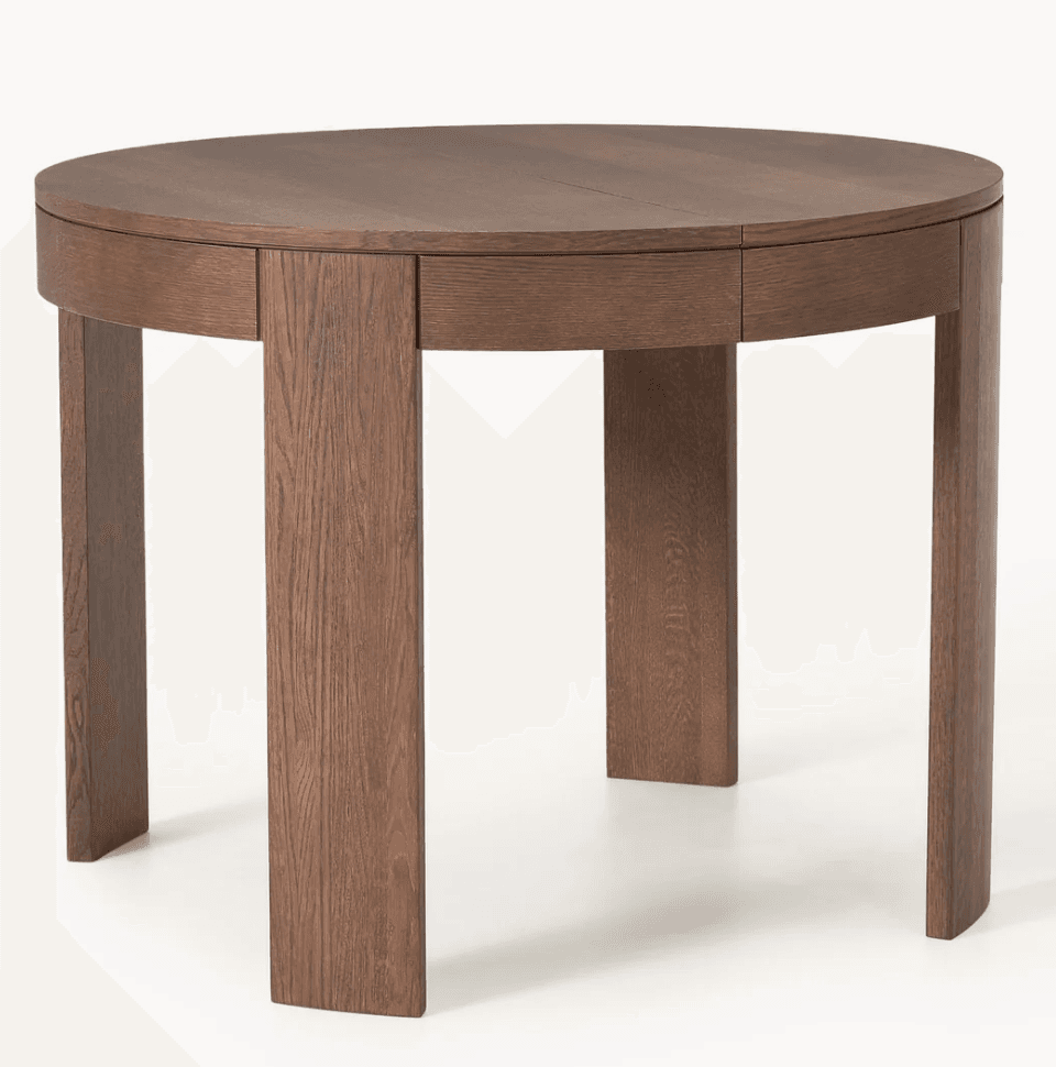 A round dining table crafted from dark oak wood, featuring a substantial tabletop with a visible seam indicating an extendable leaf. The table is supported by four wide, flat panel legs that are integrated into a thick apron beneath the tabletop. — 3D model