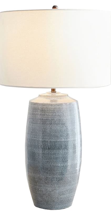 A table lamp featuring a cylindrical ceramic base with a distressed, textured grey-blue finish, topped with a plain white fabric drum shade. The base has a slightly wider top portion before tapering down to a uniform cylinder. A small metal finial secures the shade. — 3D model
