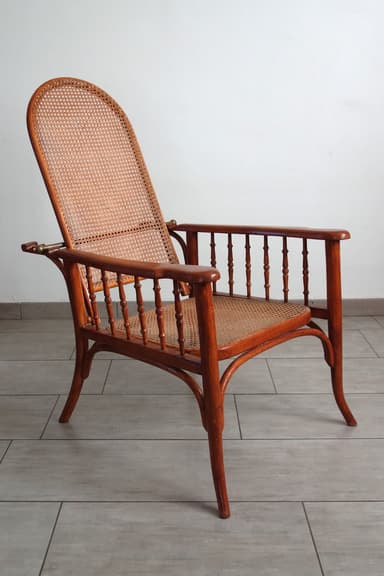 A bentwood armchair featuring a medium brown wooden frame and natural cane webbing for both the seat and the tall, arched backrest. The armrests are supported by multiple turned spindles, and the legs exhibit elegant curves characteristic of bentwood furniture. — 3D model