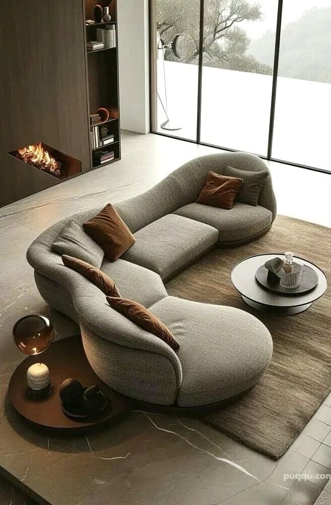 A contemporary, organically shaped sectional lounge sofa upholstered in a light grey textured fabric. The sofa features a continuous, curvilinear form with integrated backrests of varying heights, designed for multiple users. A dark, thin base trim follows the sinuous outline of the piece. Two loose accent pillows, one grey and one brown, are placed on the seating surface. — 3D model