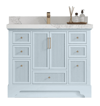 A light blue bathroom vanity featuring a white marble countertop with an integrated rectangular sink and an attached backsplash. The cabinet base has ribbed detailing on its drawer and door fronts, accented with gold-finished hardware (knobs and pulls). A gold single-handle faucet is mounted on the countertop. Decorative bathroom accessories are placed on a wooden tray to the right of the sink. — 3D model