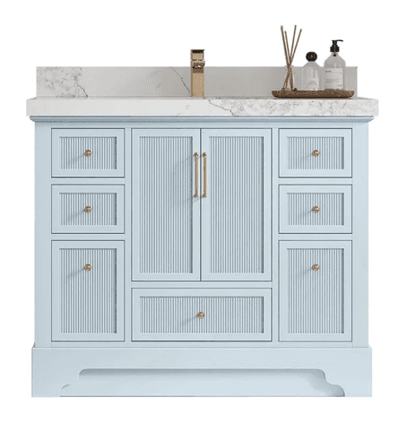 A light blue bathroom vanity featuring a white marble countertop with an integrated rectangular sink and an attached backsplash. The cabinet base has ribbed detailing on its drawer and door fronts, accented with gold-finished hardware (knobs and pulls). A gold single-handle faucet is mounted on the countertop. Decorative bathroom accessories are placed on a wooden tray to the right of the sink. — 3D model