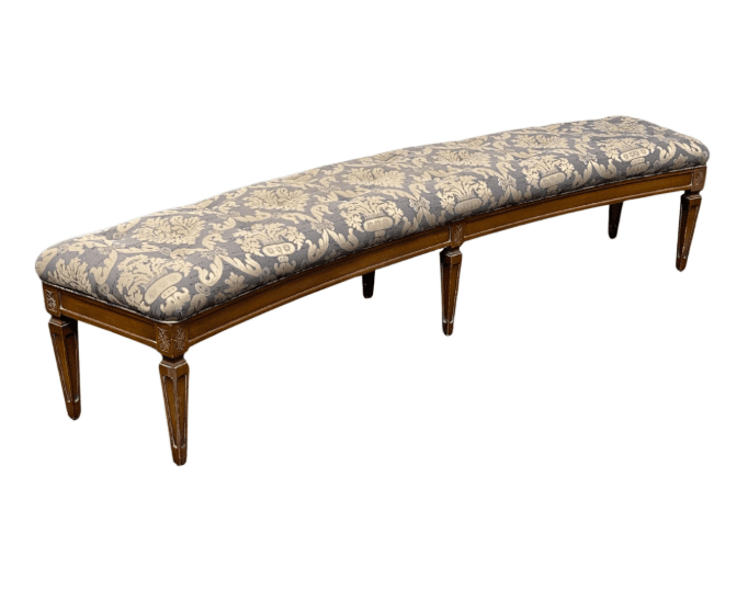 A long, upholstered bench with a patterned fabric. The bench has a wooden frame and four tapered legs, each with decorative carved details near the top. The upholstery features a damask-like pattern in grey and gold tones. — 3D model