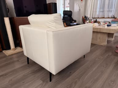 A modern white sofa with a tufted backrest and armrests, upholstered in a material that appears to be faux leather or high-quality vinyl. It features a clean, minimalist design with slim, black metal legs. The stitching detail is visible along the edges. — 3D model