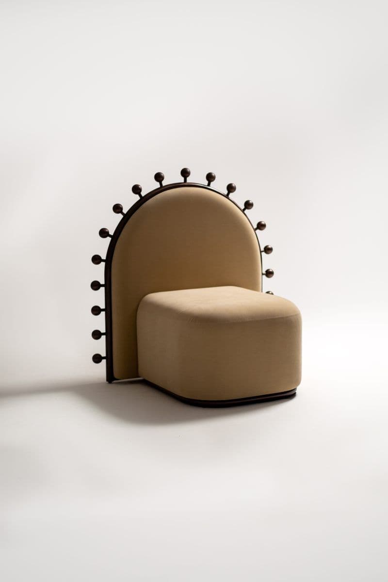 An unusual armless accent chair featuring a plush, beige upholstered seat and an tall, arched backrest. The backrest is framed by a dark, possibly metal or wood, structure adorned with evenly spaced spherical finials along its top and sides. The base of the chair also features a dark, matching trim. — 3D model