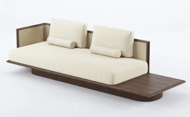 A low-profile sofa featuring a wooden base with an extended side surface. The seating area is upholstered in a textured cream fabric. It is equipped with two large back cushions and two smaller cylindrical bolster cushions. The back of the sofa incorporates woven cane panels framed by dark wood. — 3D model