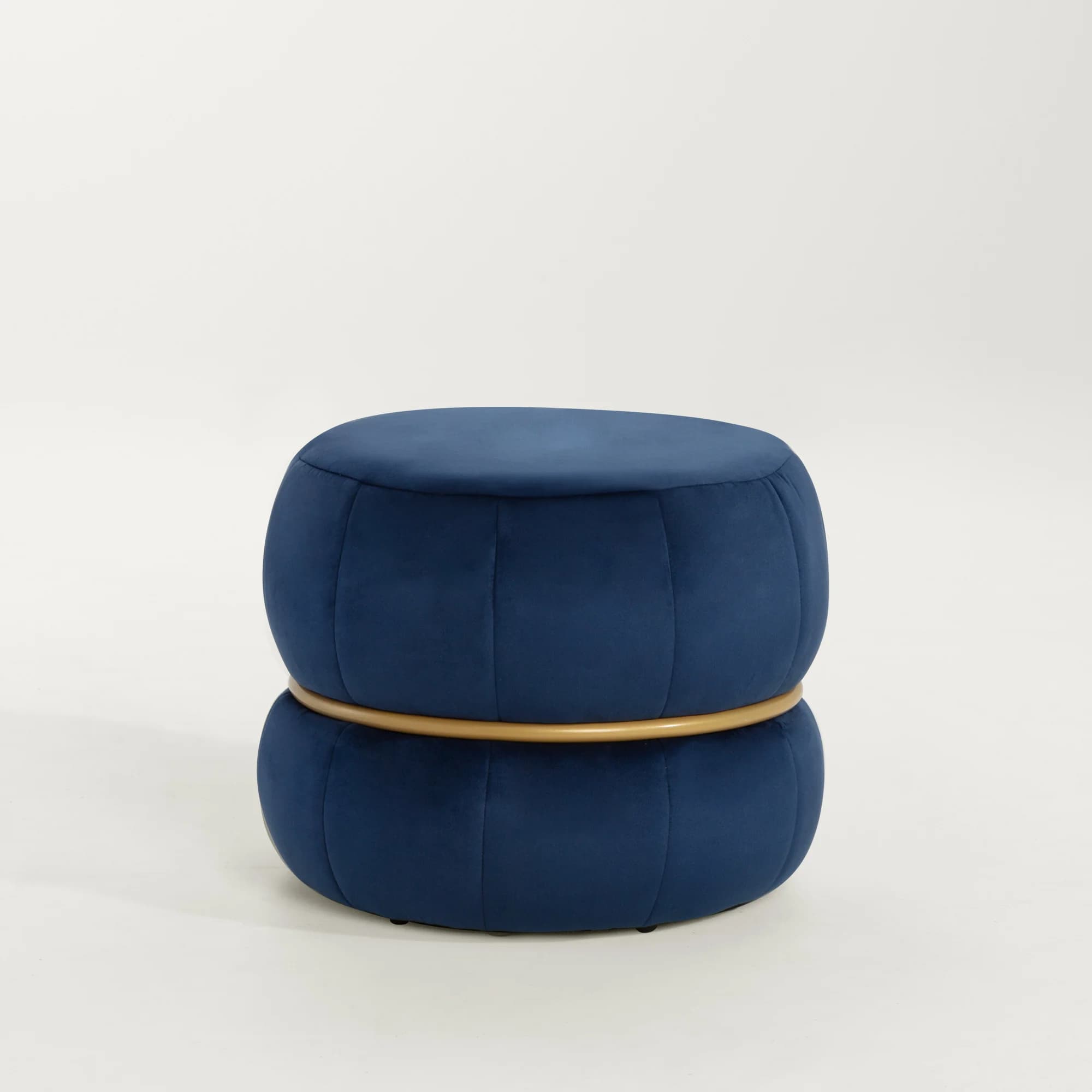 A round ottoman upholstered in a dark blue velvet fabric. The upholstery features vertical channel tufting, creating a segmented, gourd-like appearance. A thin, metallic gold band encircles the ottoman horizontally, separating the upper and lower sections of the tufting. The overall shape is cylindrical with rounded top and bottom edges. — 3D model