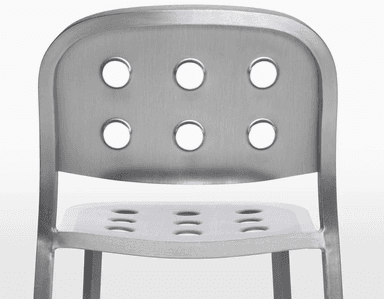 A modern chair with a brushed aluminum finish. It features a curved backrest and seat, both perforated with a pattern of six circular holes each. The chair has four slender, straight legs that taper slightly towards the bottom. — 3D model