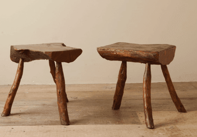 A rustic three-legged stool with an irregular, organic-shaped seat. The seat appears to be made from a single piece of wood with a natural edge. The legs are rough, unfinished branches, joined directly to the underside of the seat. — 3D model