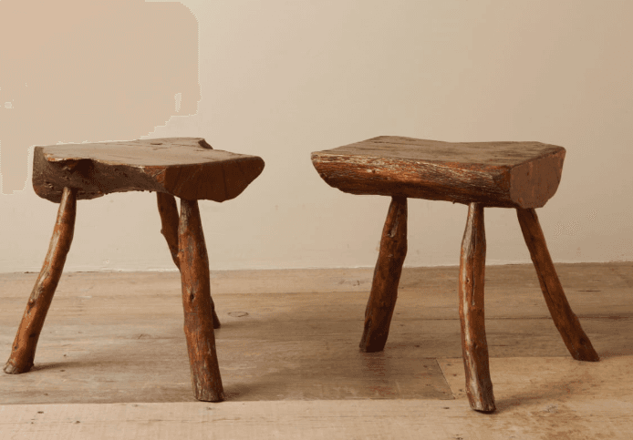 A rustic three-legged stool with an irregular, organic-shaped seat. The seat appears to be made from a single piece of wood with a natural edge. The legs are rough, unfinished branches, joined directly to the underside of the seat. — 3D model