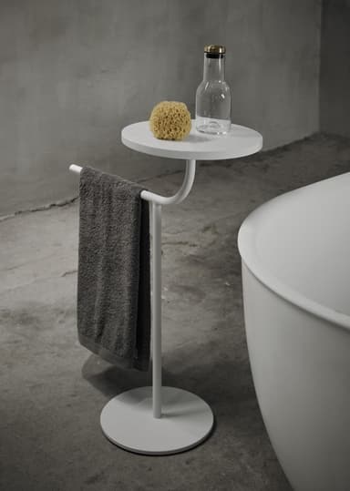 A minimalist white pedestal accent table featuring a round tabletop, a slender central column, and a circular base. An integrated handle or rail extends from beneath the tabletop, curving slightly upwards. The entire piece is rendered in a uniform matte white finish, suggesting a powder-coated metal construction, and is presented against a plain white background. — 3D model