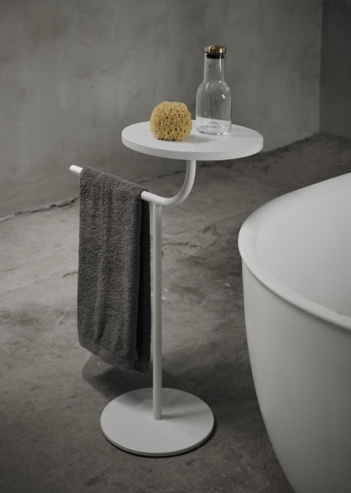 A minimalist white pedestal accent table featuring a round tabletop, a slender central column, and a circular base. An integrated handle or rail extends from beneath the tabletop, curving slightly upwards. The entire piece is rendered in a uniform matte white finish, suggesting a powder-coated metal construction, and is presented against a plain white background. — 3D model