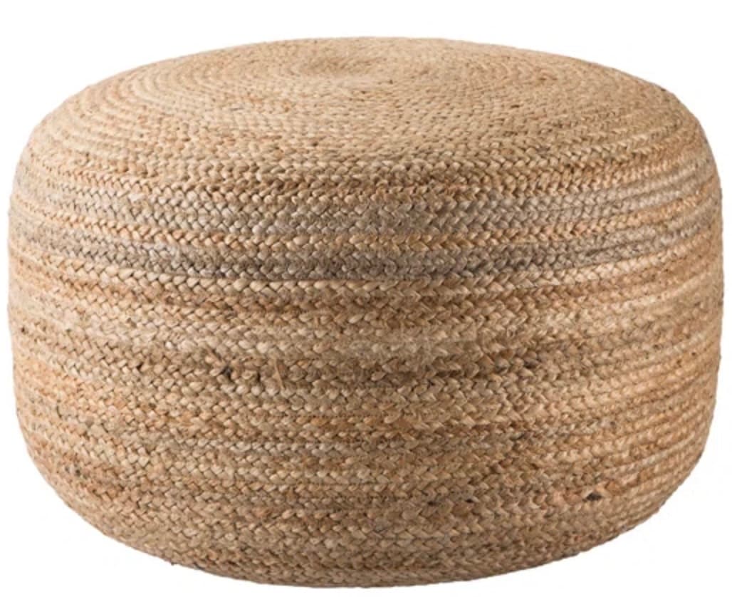 A round, cylindrical ottoman upholstered in woven jute. The texture is coarse and natural, with variations in color due to the natural fibers. The weaving pattern is visible on both the top and sides, creating a visually textured surface. — 3D model