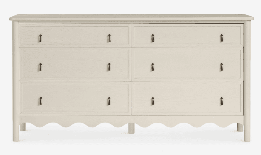 A contemporary light gray double dresser featuring six drawers, arranged in two columns of three. The bottom edge of the dresser has a distinctive scalloped design, and each drawer is fitted with a simple, dark-toned pull handle. The dresser stands on four rounded legs, and its top surface has softly rounded corners. — 3D model