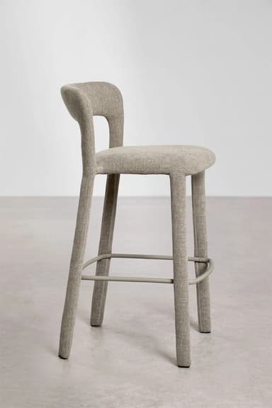 A modern bar stool with a slightly curved backrest and a seat upholstered in a textured beige fabric. The stool has four tapered legs that extend upwards to form the seat and backrest structure. Metal footrests are integrated between the legs. — 3D model