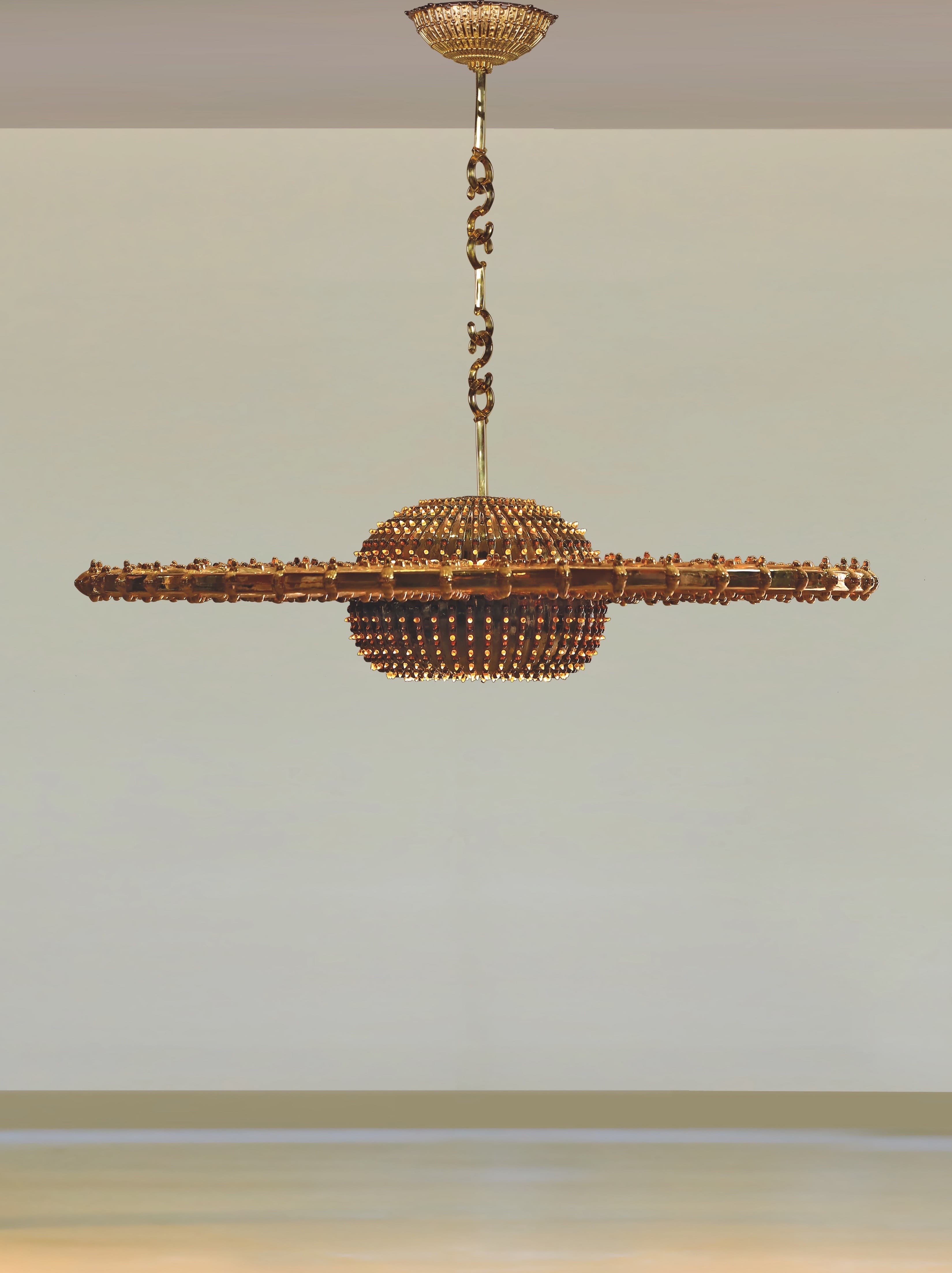A highly ornate ceiling-mounted chandelier featuring a gold-toned metal construction. It consists of a central, dome-shaped body surrounded by a wide, flat, circular ring, reminiscent of Saturn. Both the central body and the ring are densely embellished with numerous small, reflective elements, likely crystals or glass beads, which create a shimmering effect. The chandelier is suspended from the ceiling by a decorative link chain and a central rod, attached to an ornate ceiling canopy. — 3D model