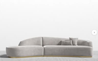 A contemporary curved modular sofa upholstered in light gray velvet, featuring an integrated backrest and armrests, supported by a recessed polished brass plinth base. It includes two matching throw pillows. — 3D model