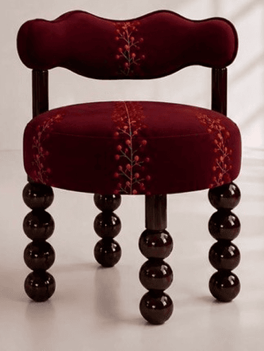 A compact, upholstered decorative accent chair featuring a distinctive burgundy velvet-like fabric. The chair has a rounded, plush seat and a low, scalloped backrest that integrates subtle arm supports. Both the seat and backrest are adorned with an embroidered pattern depicting berry branches in shades of orange, red, and gold. The chair stands on four dark brown, lacquered wooden legs, each composed of a series of stacked spherical elements, commonly known as bobbin or spool legs. — 3D model
