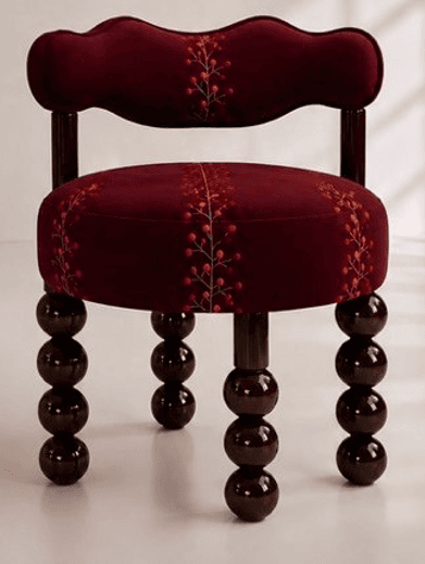 A compact, upholstered decorative accent chair featuring a distinctive burgundy velvet-like fabric. The chair has a rounded, plush seat and a low, scalloped backrest that integrates subtle arm supports. Both the seat and backrest are adorned with an embroidered pattern depicting berry branches in shades of orange, red, and gold. The chair stands on four dark brown, lacquered wooden legs, each composed of a series of stacked spherical elements, commonly known as bobbin or spool legs. — 3D model