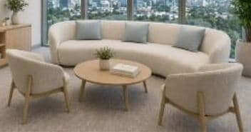 A modern living room furniture set featuring a curved, cream-colored boucle sofa with three light blue cushions, two matching cream boucle armchairs with light wooden frames, and a round light wooden coffee table adorned with a small plant and books. — 3D model