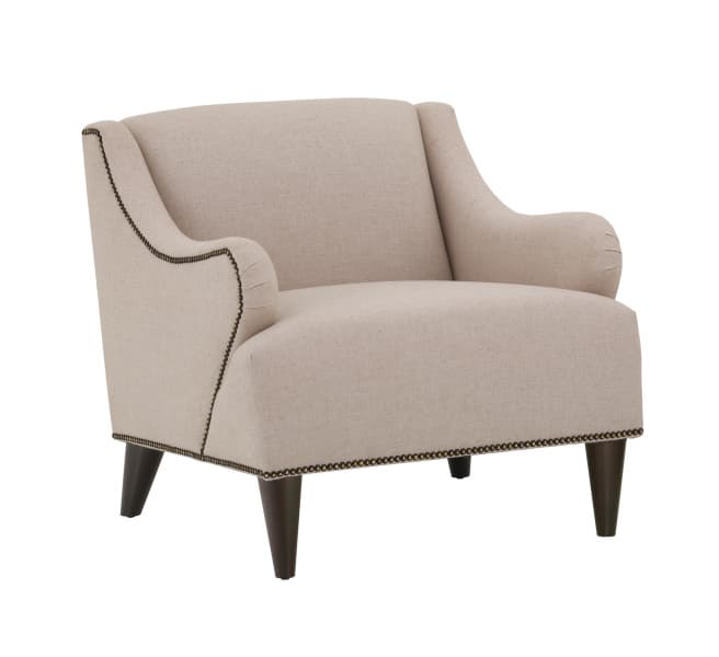 A beige upholstered armchair with dark wooden legs. The armchair features a high back that curves into winged sides, and rolled arms. Decorative nailhead trim runs along the edges of the upholstery, accentuating the silhouette. — 3D model