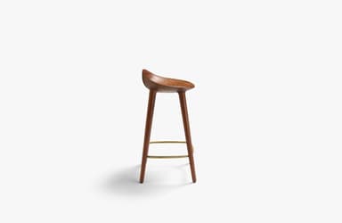 A modern bar stool crafted from dark brown wood, likely walnut, featuring a deeply sculpted saddle seat for ergonomic comfort. It stands on four slender, tapered legs that splay slightly outwards, connected by a triangular brass-toned metal footrest. The design is minimalist and contemporary, highlighting the natural beauty of the wood grain. — 3D model