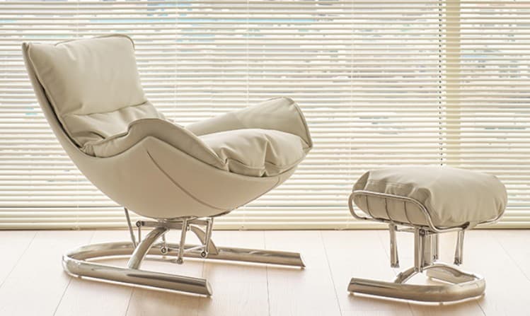 A cream-colored lounge chair featuring a plush, upholstered body set on a polished metal sled base. The chair's form provides a relaxed, reclined seating position with integrated armrests and ample cushioning. The base is constructed from curved metal tubing, providing a stable yet visually light foundation. — 3D model
